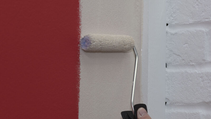 A mini paint roller being used to paint a wall white.